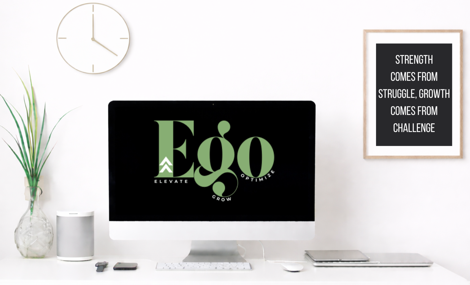 A white office desk with a large iMac computer displaying a logo with the words "Elevate, Grow, Optimize" surrounding the word "Eco" in green. To the left, there's a glass vase with green plants and a small white smart speaker. On the right, a framed black and white motivational quote says, "Strength comes from struggle, growth comes from challenge." A computer mouse, a keyboard, and a closed laptop are on the desk. The background features a white wall with a round wall clock.