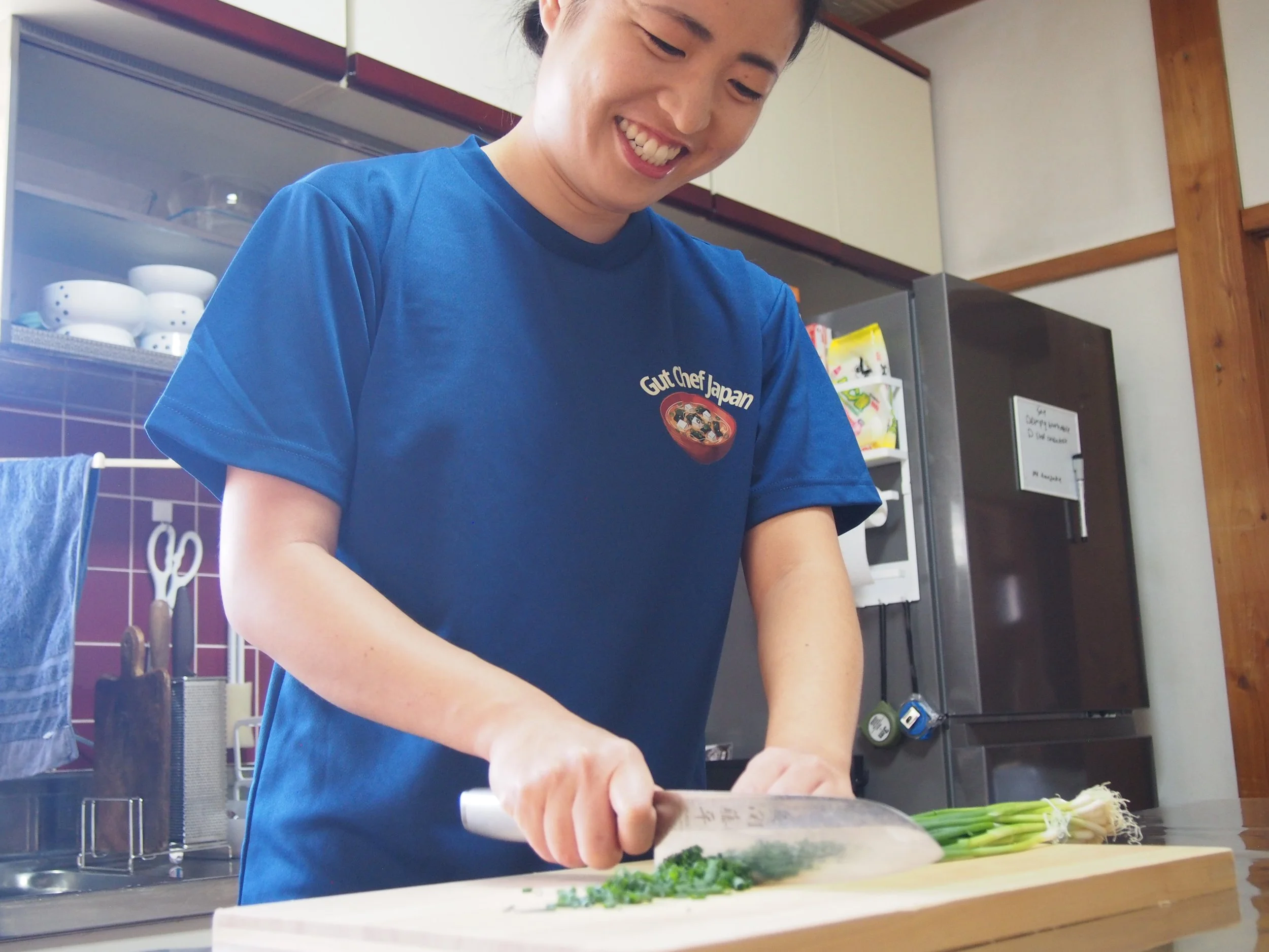A woman wearing a blue shirt with 'Gut Chef Japan' logo preparing vegetables in a kitchen.