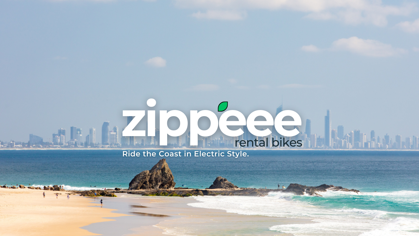 A beach with a city skyline in the background, rocks in the water, and a few people walking on the sand, with the text 'zippee rental bikes Ride the Coast in Electric Style.' overlaid.