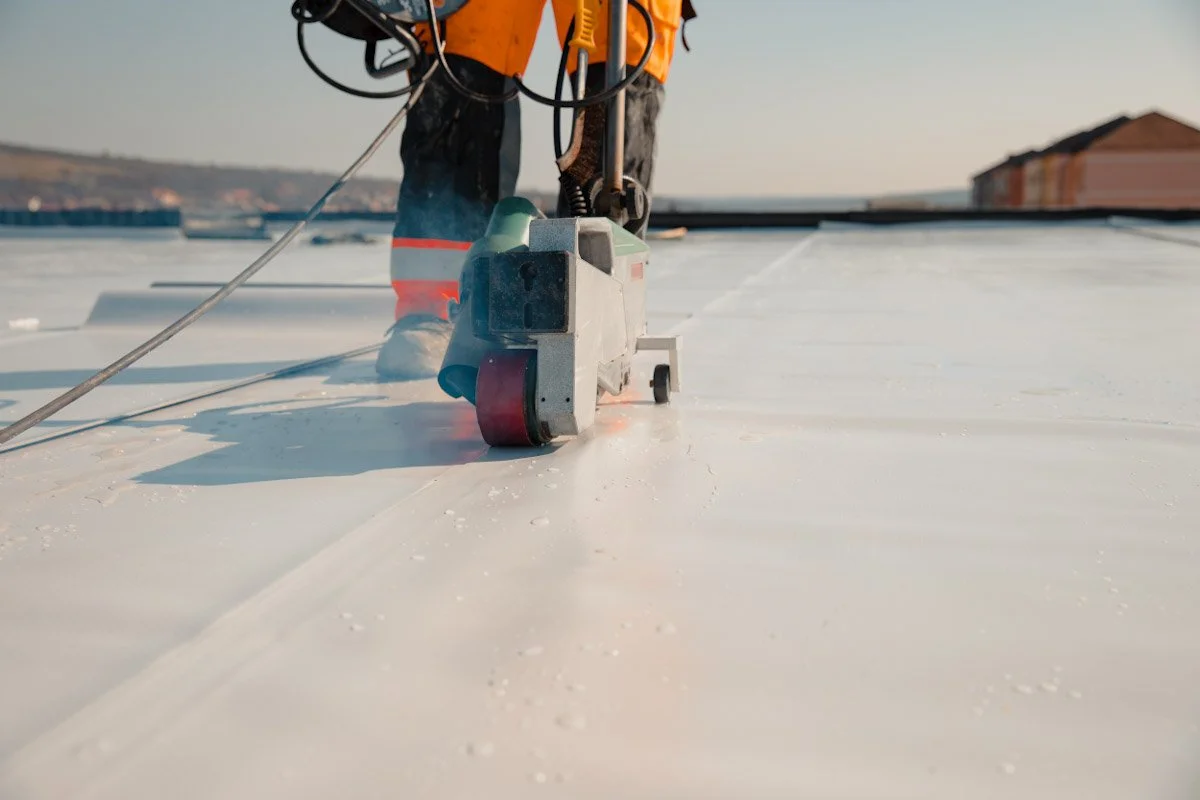 Worker using a cutting tool on a flat, white rooftop under clear skies.