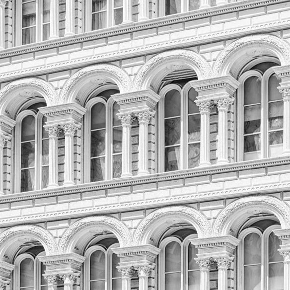 Close-up of a historic building facade featuring arched windows and ornate Corinthian columns in black and white.
