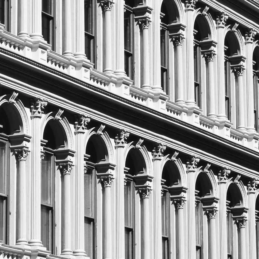 Black and white photo of an ornate classical building facade featuring tall columns, arches, and elaborate decorative details.