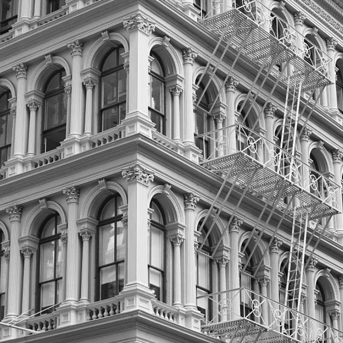 Black and white photo of a historic building with ornate architectural details and fire escape balconies on each floor.