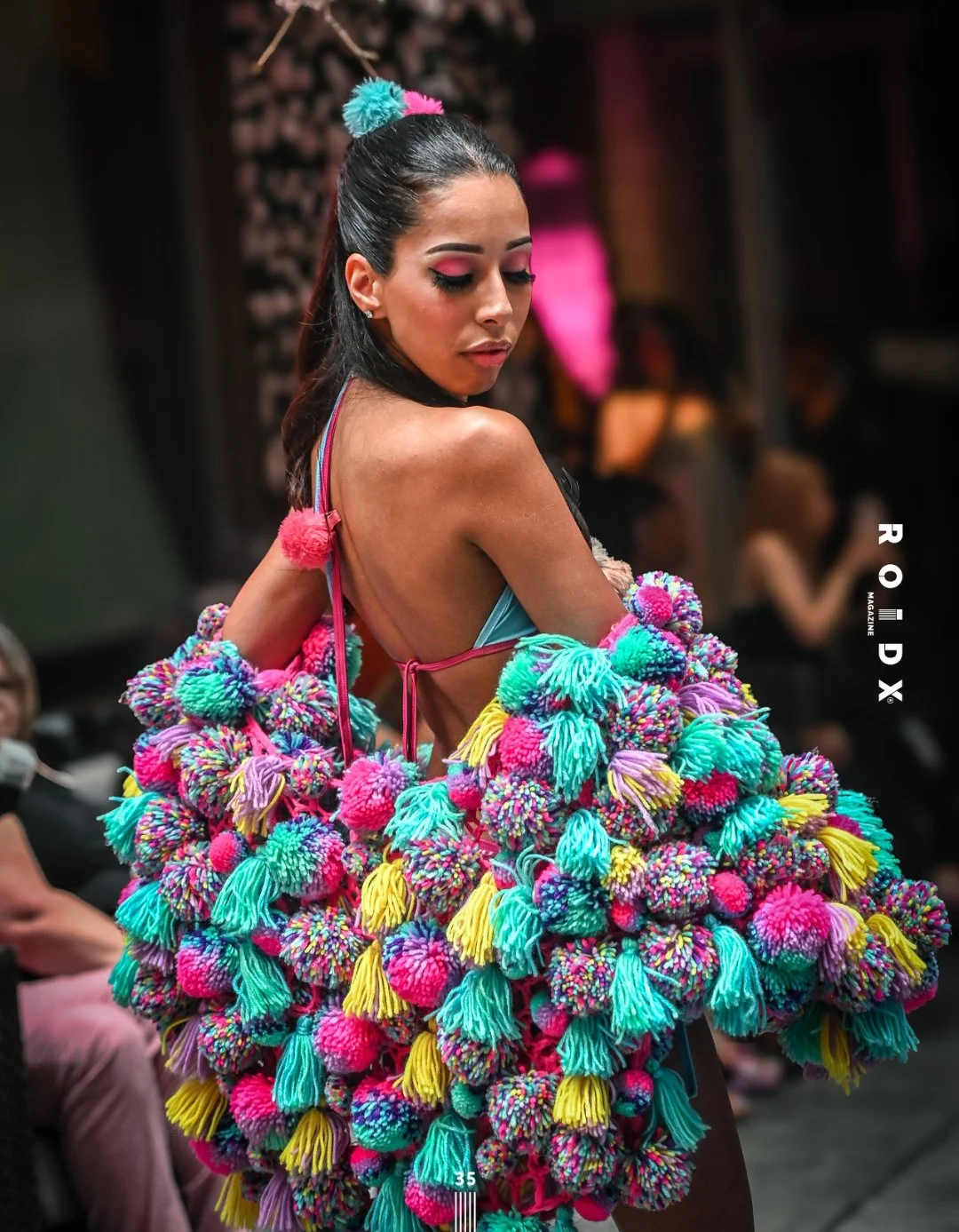 A woman wearing a colorful pom-pom dress at a fashion event.