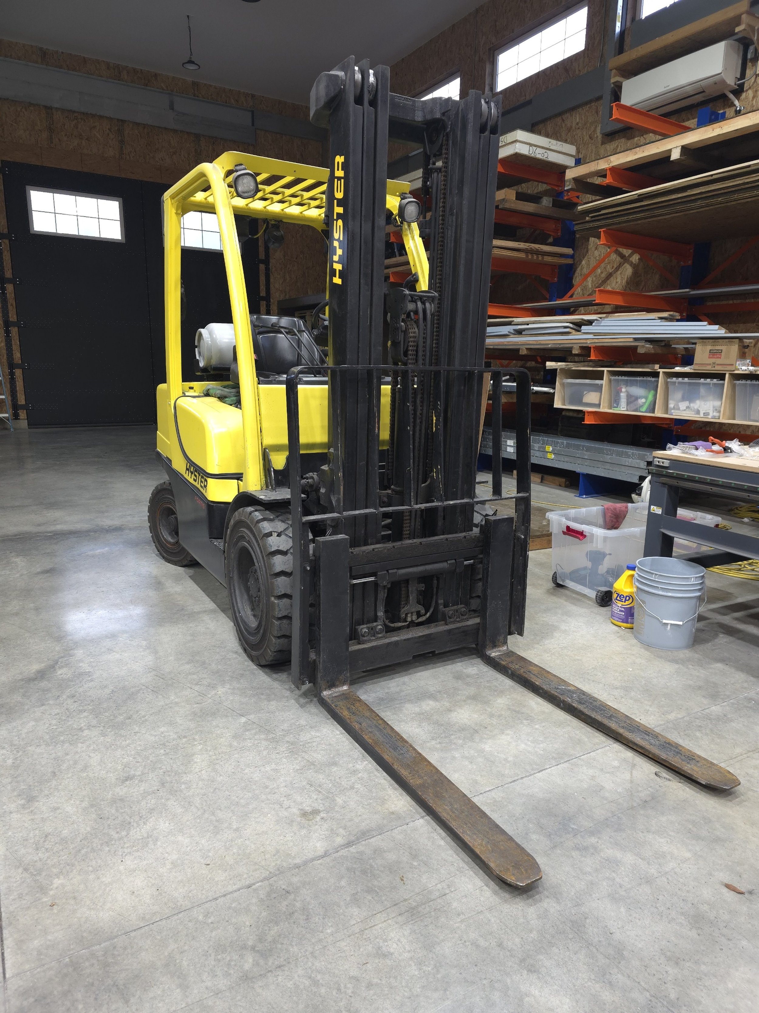 Yellow Hyster forklift inside a warehouse with shelving and storage bins.
