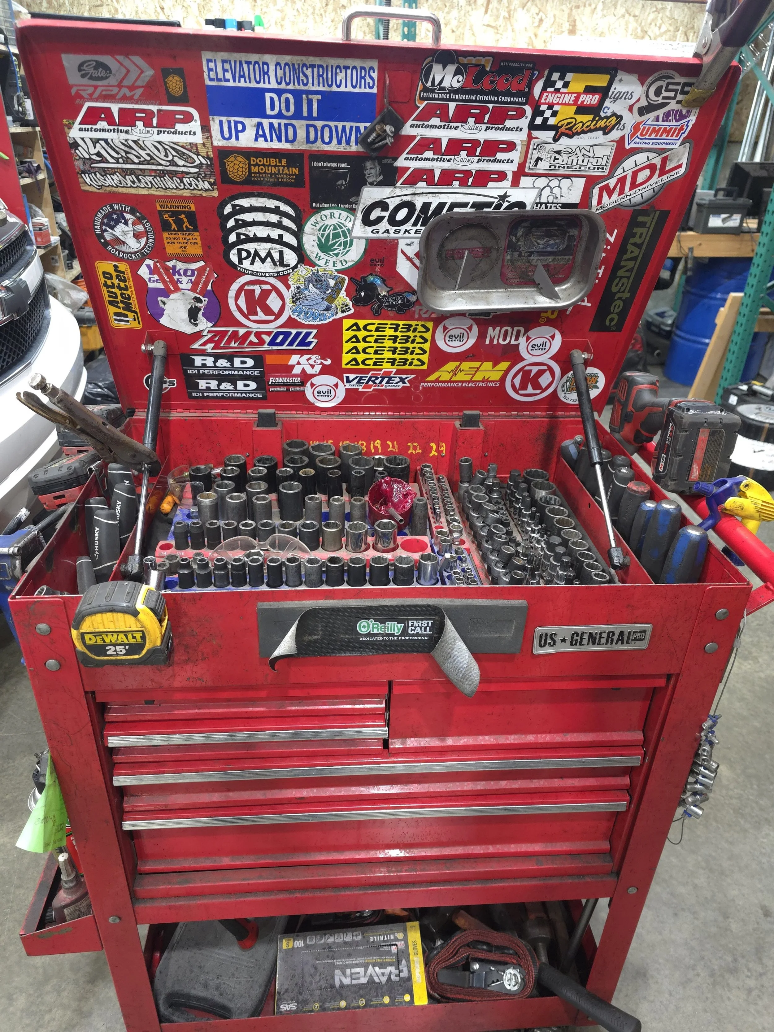 Red tool chest with organized socket sets and various tools, with numerous automotive and racing stickers on the inside of the lid.