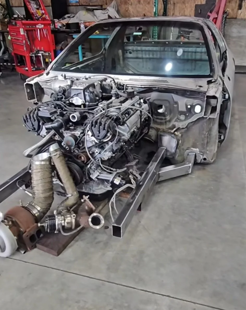 Disassembled car inside a garage with engine and turbocharger components visible.
