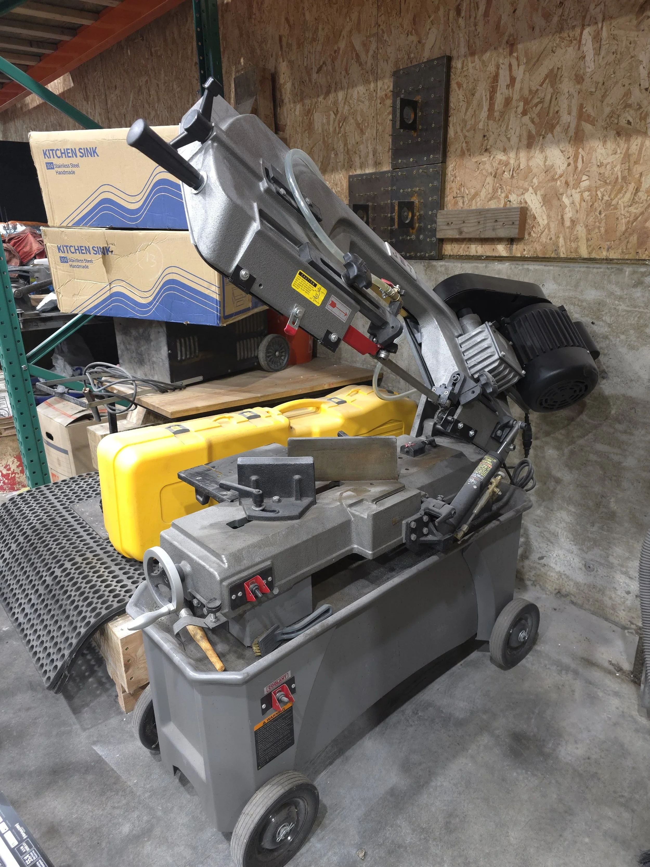 Industrial metal chop saw on a cart in a workshop setting.