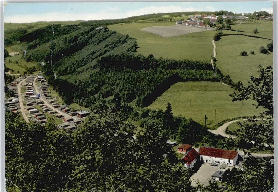 Landschaft mit Wäldern, Wiesen, Landstraßen, Wohnhäusern und einem Parkplatz im Vordergrund.