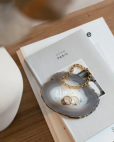 Gold bracelet and rings on a ceramic dish placed on an open book on a wooden table.