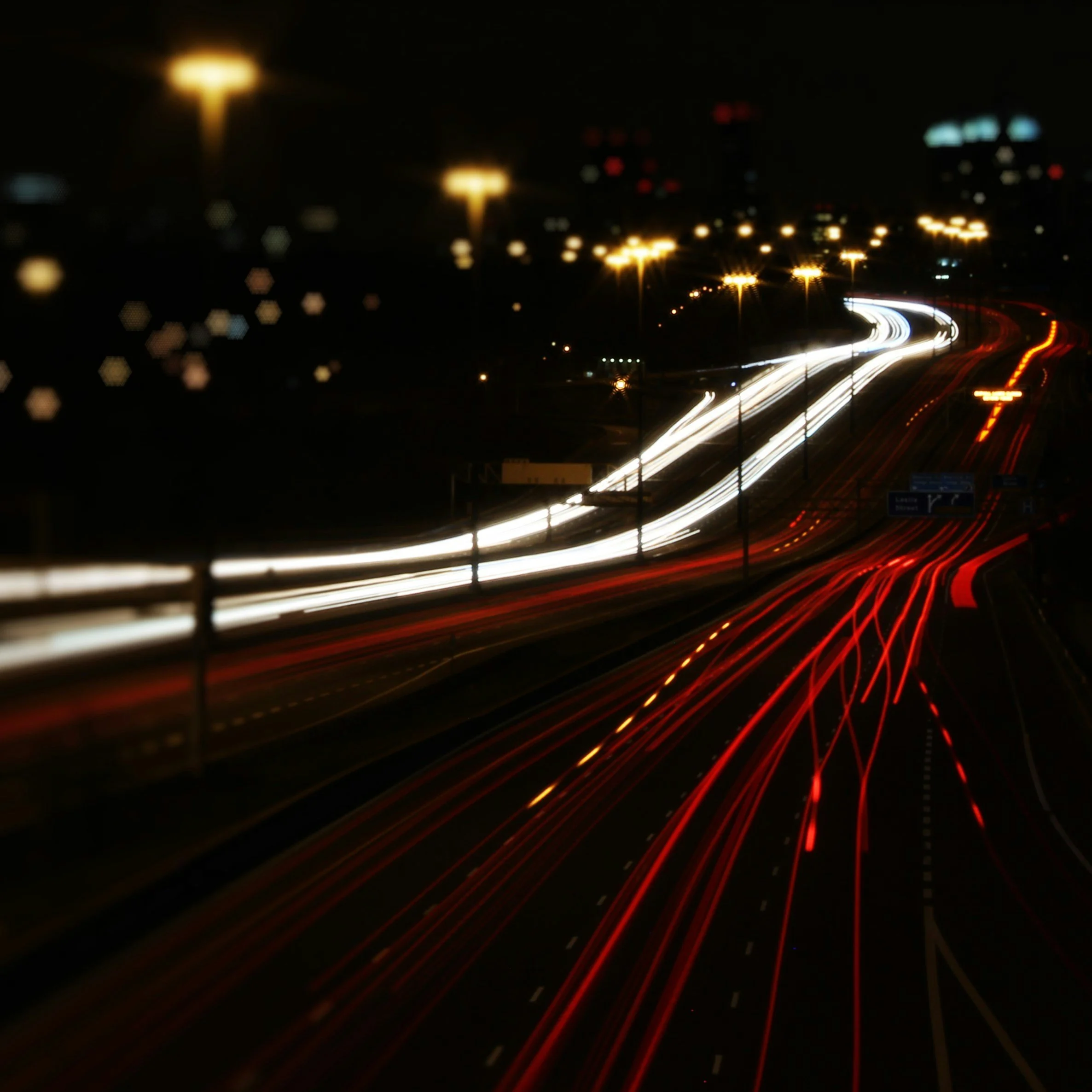 Nighttime highway with streaks of light from moving vehicles, showing white and red light trails and illuminated streetlights.