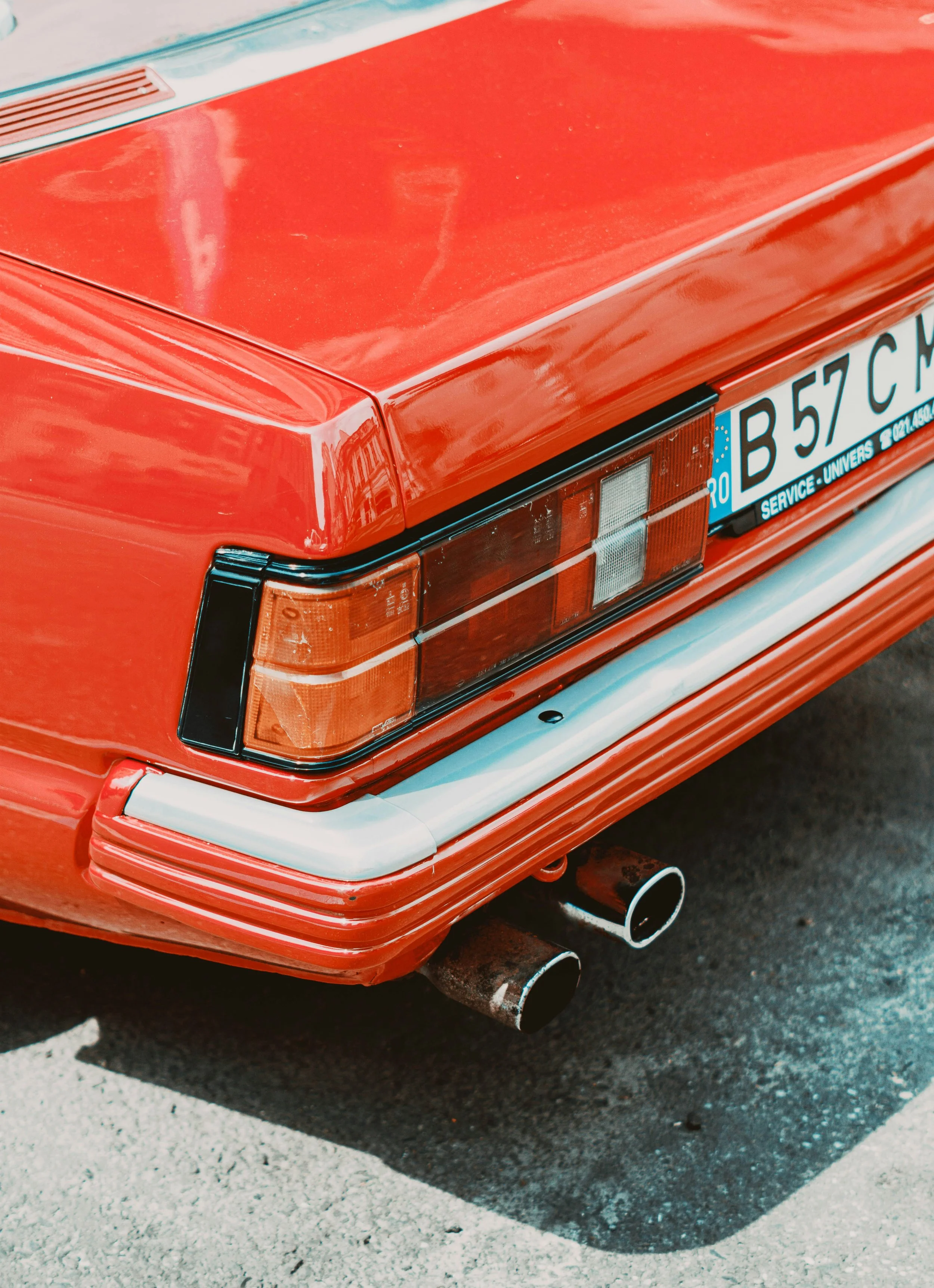 Close-up of the rear end of a vintage red car, showing tail light, dual exhaust pipes, and a European license plate.