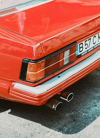 Close-up of the rear end of a vintage red car with dual exhaust pipes.