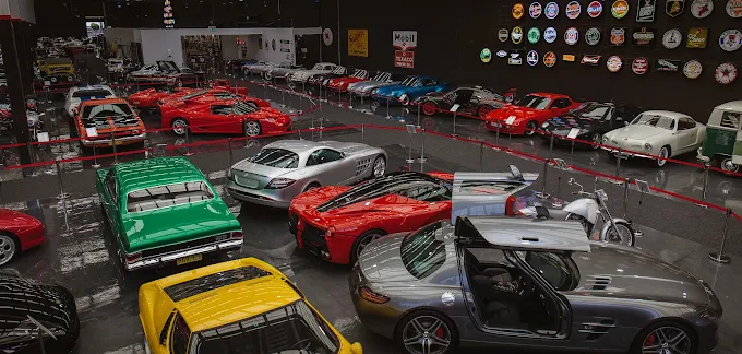 Classic and modern cars on display in a car museum with vintage signs and memorabilia.