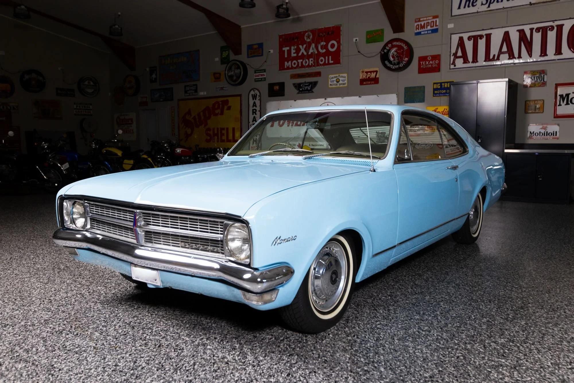 Light blue vintage Mercury Cougar car in a garage decorated with automotive signs and motorcycle models
