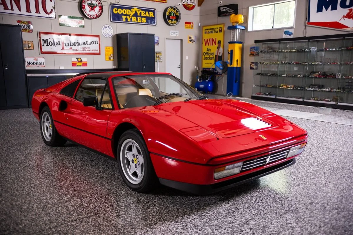 A red vintage Ferrari sports car is parked inside a garage decorated with automotive signs and collectibles.