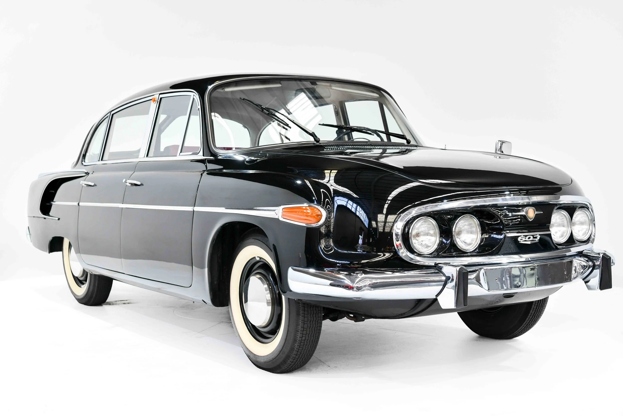 A classic black car with chrome trim and whitewall tires, parked indoors with a plain white background.