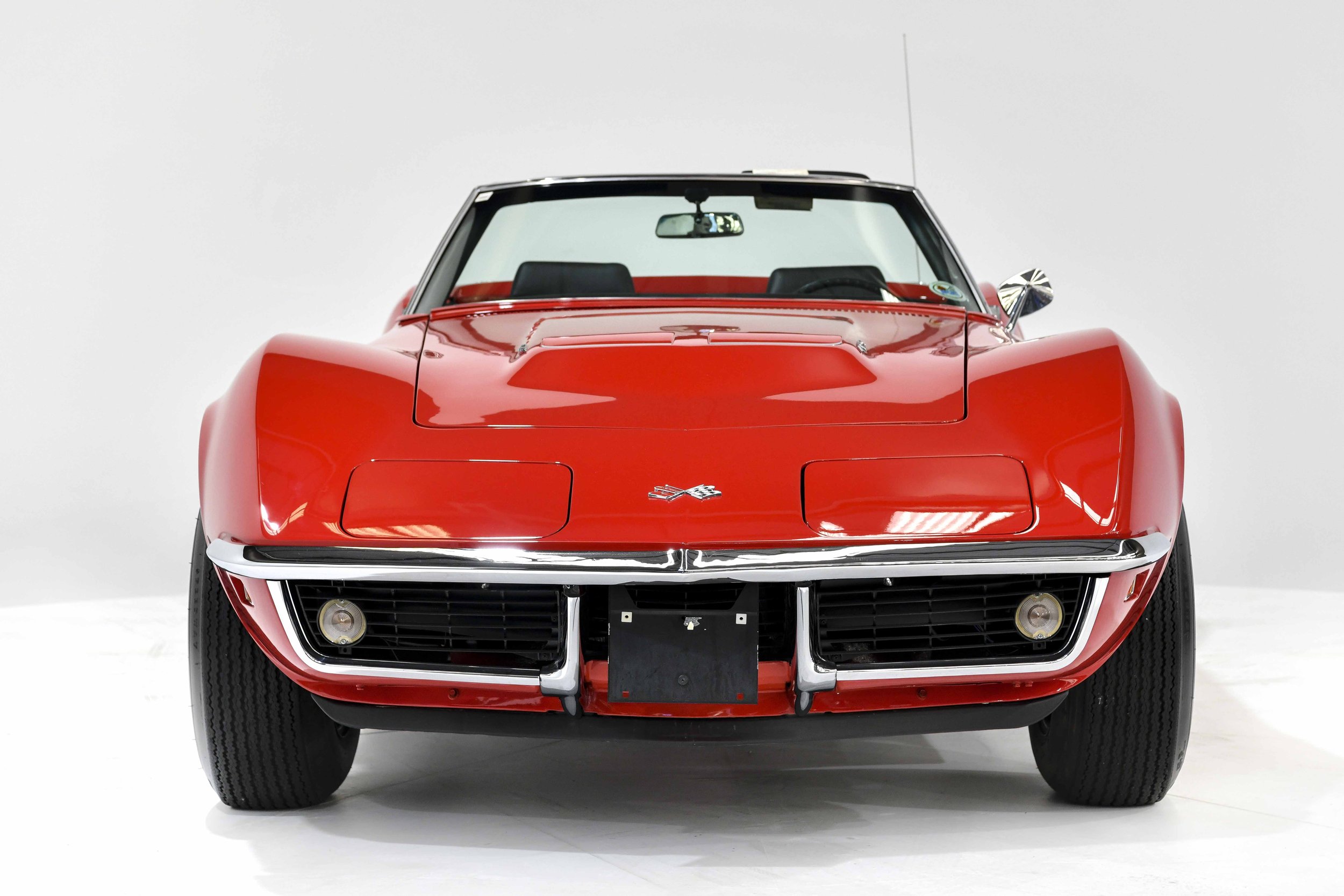 Red vintage Chevrolet Corvette with black interior, front view, on a plain light background.