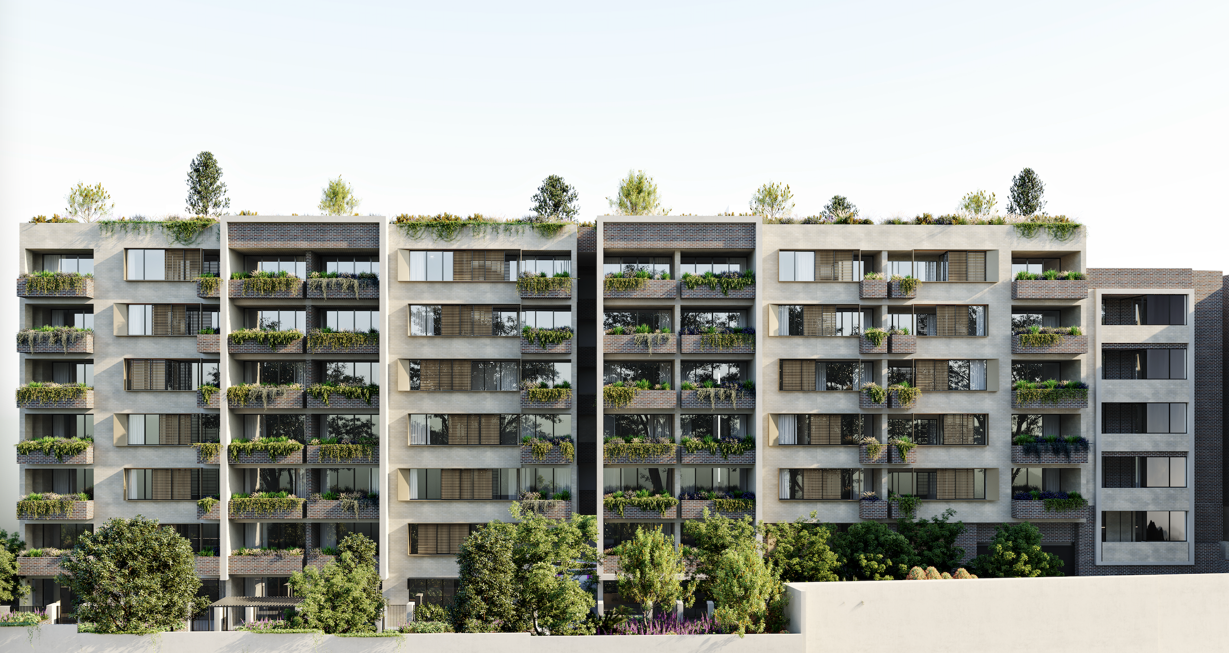 Modern multi-story apartment building with balconies decorated with plants and greenery, trees and shrubs in front, and a clear sky overhead.
