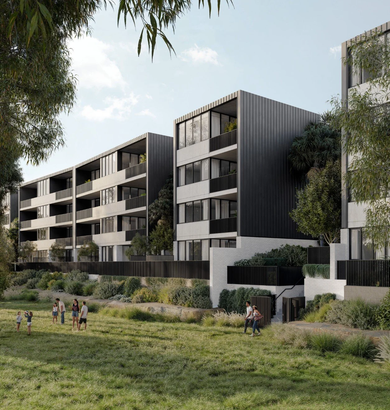 Modern apartment buildings with large balconies and black metal siding, set against a clear sky, with a grassy area in the foreground where people are walking and children are playing.