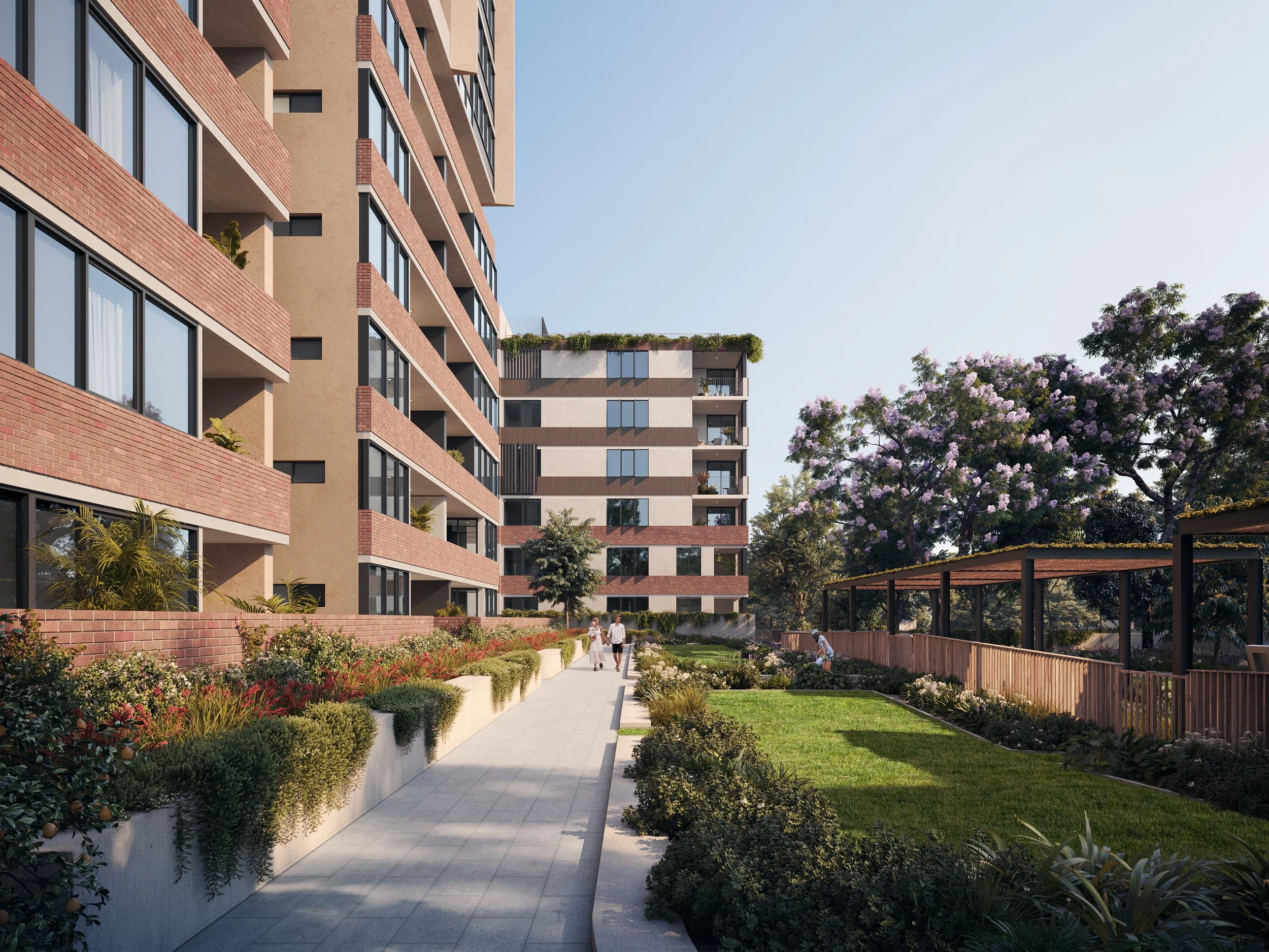 A modern residential apartment complex with multiple stories, large windows, and balconies. The building is surrounded by well-maintained gardens, trees, and a paved pathway with people walking. There is an outdoor seating area with a wooden fence on