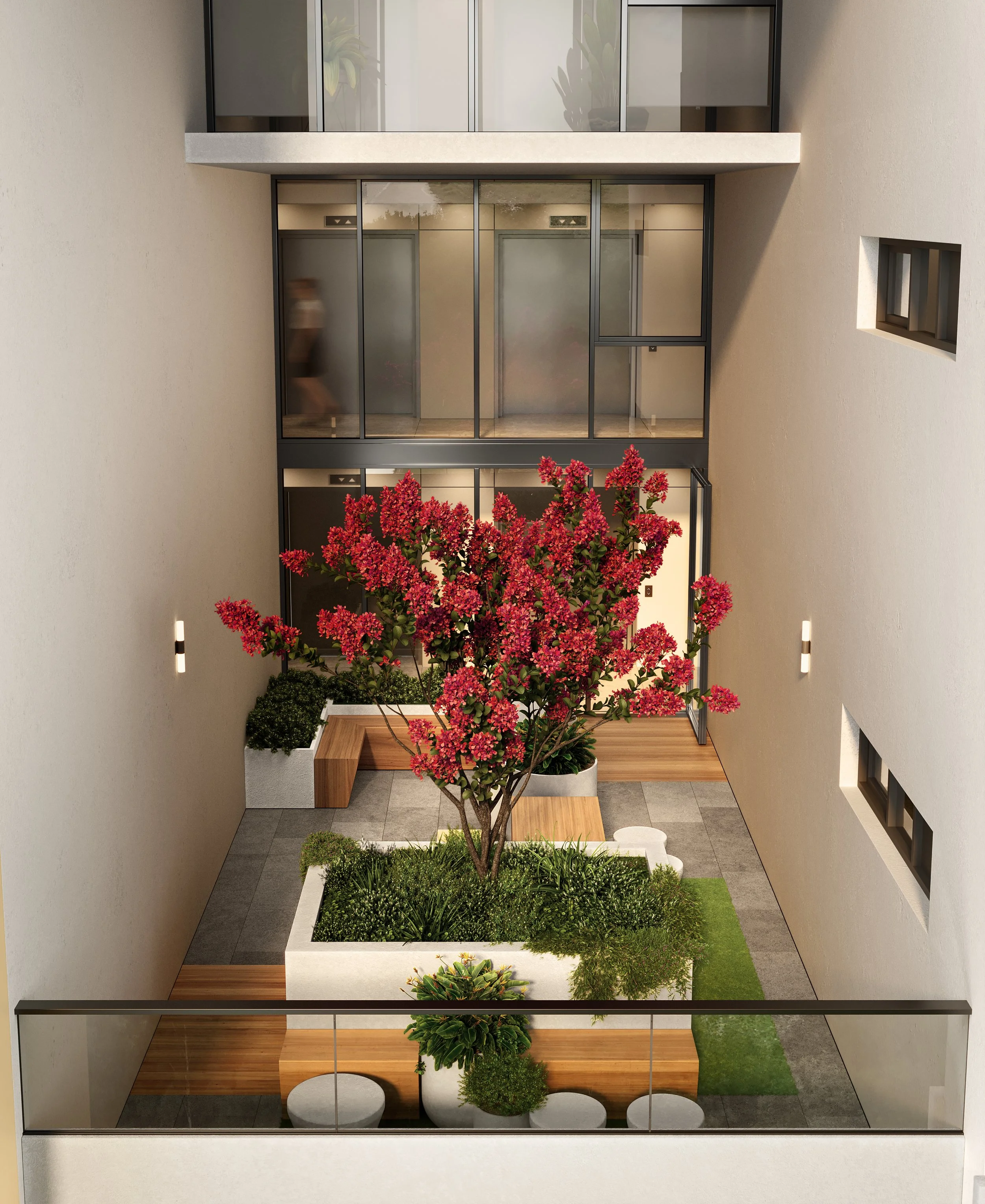 Interior view of a modern apartment courtyard with a central pink-flowering tree, seating, and glass elevators in the background.