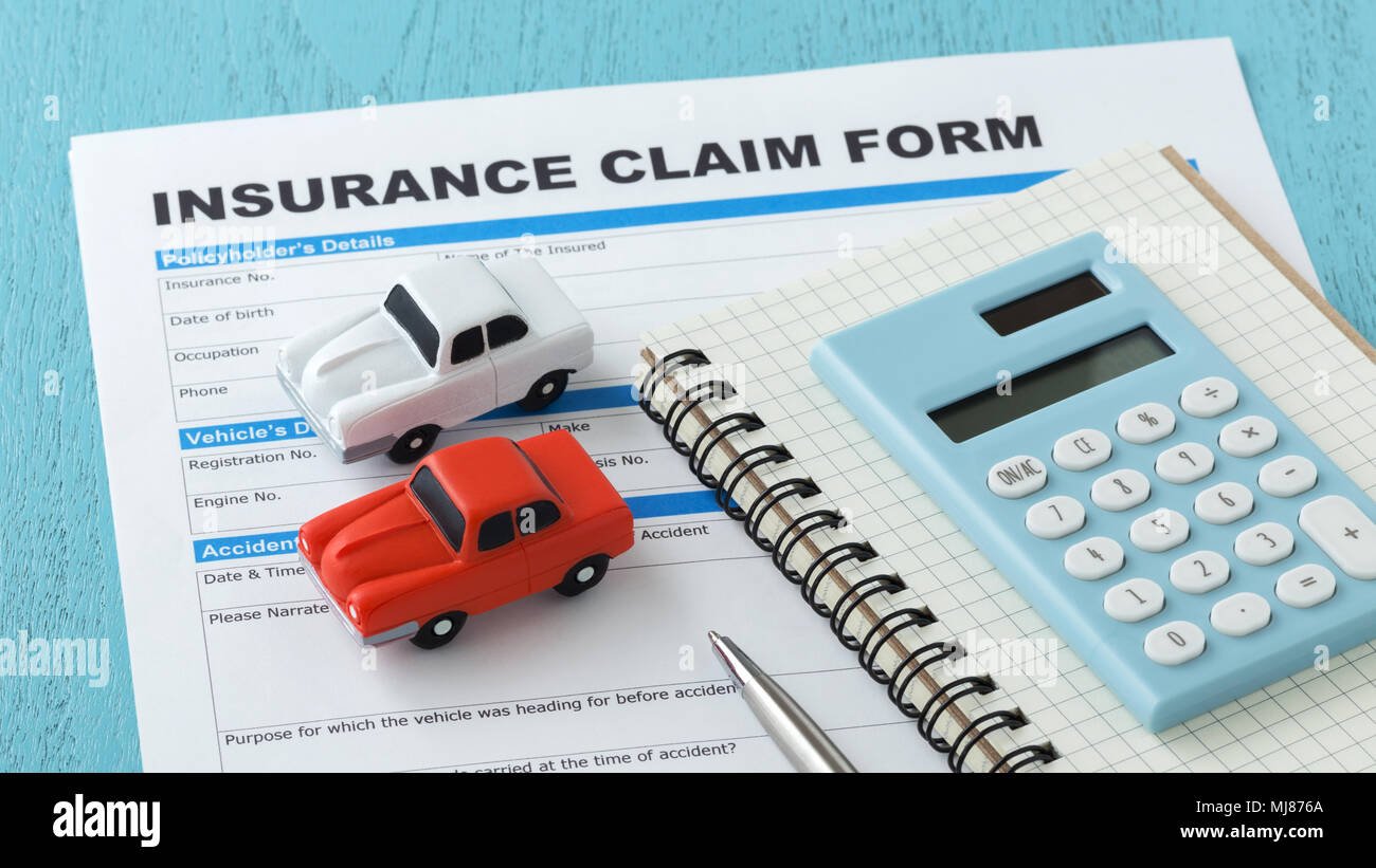 Insurance claim form with two toy cars, a calculator, a notebook, and a pen on a blue surface.