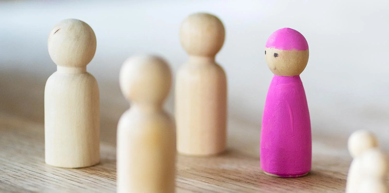 Holzfiguren, davon eine pink bemalt, auf einem Holztisch.