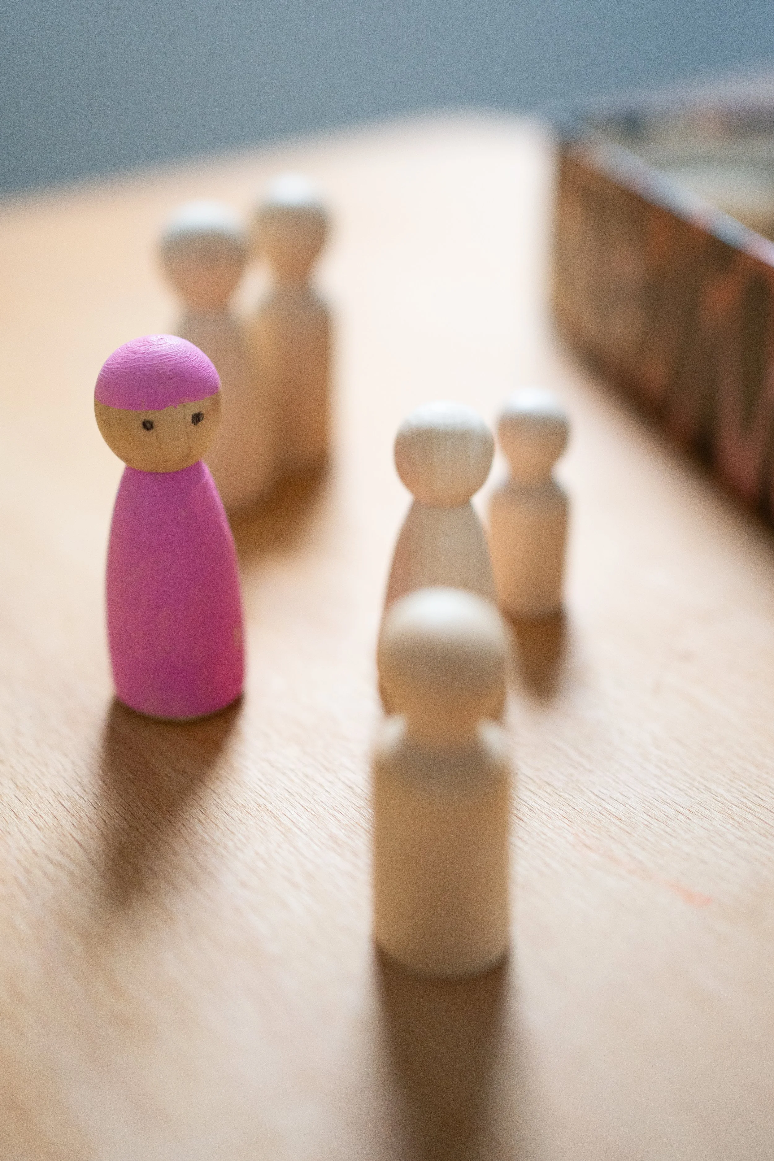 Holzfiguren, darunter eine pinke Figur mit Gesicht, stehen auf einem Tisch in einem Raum.