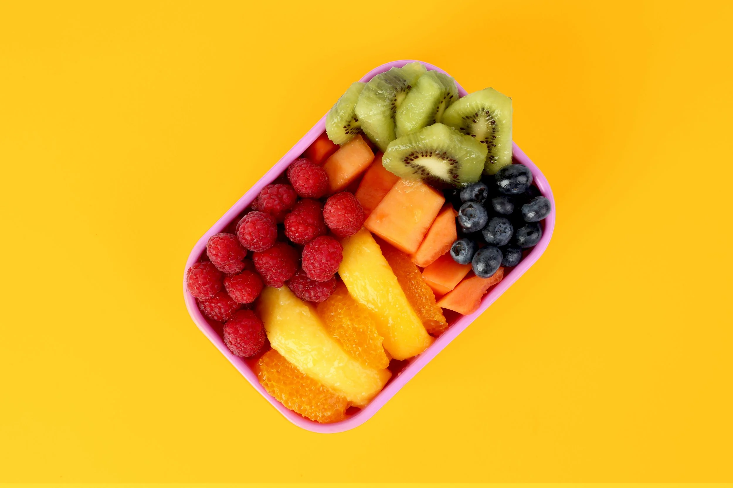 Lunchbox full of sliced fruit and berries.