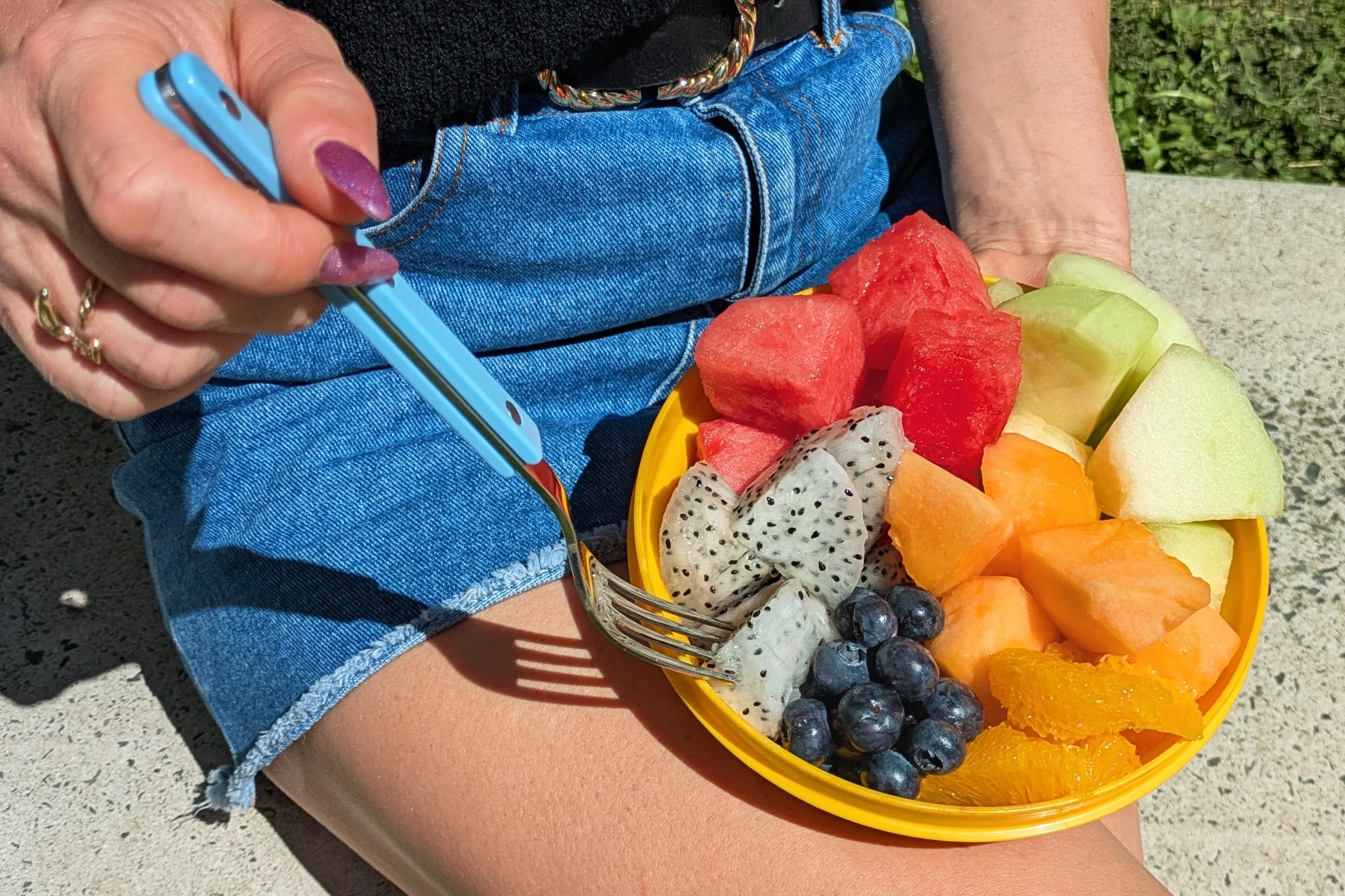 Person eating a bowl of fruit with a fork.