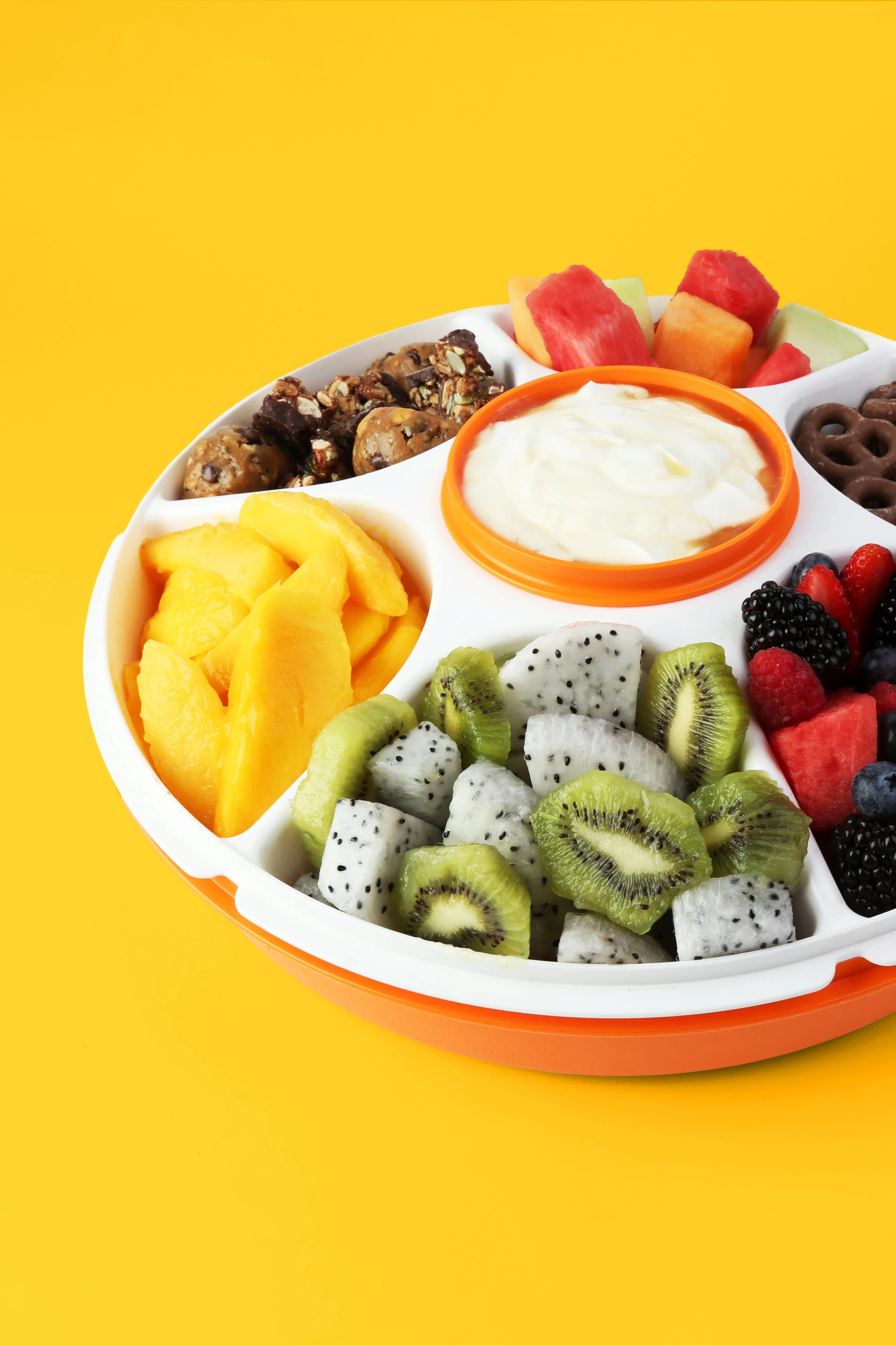 Platter of sliced fruit and snacks on a yellow background.