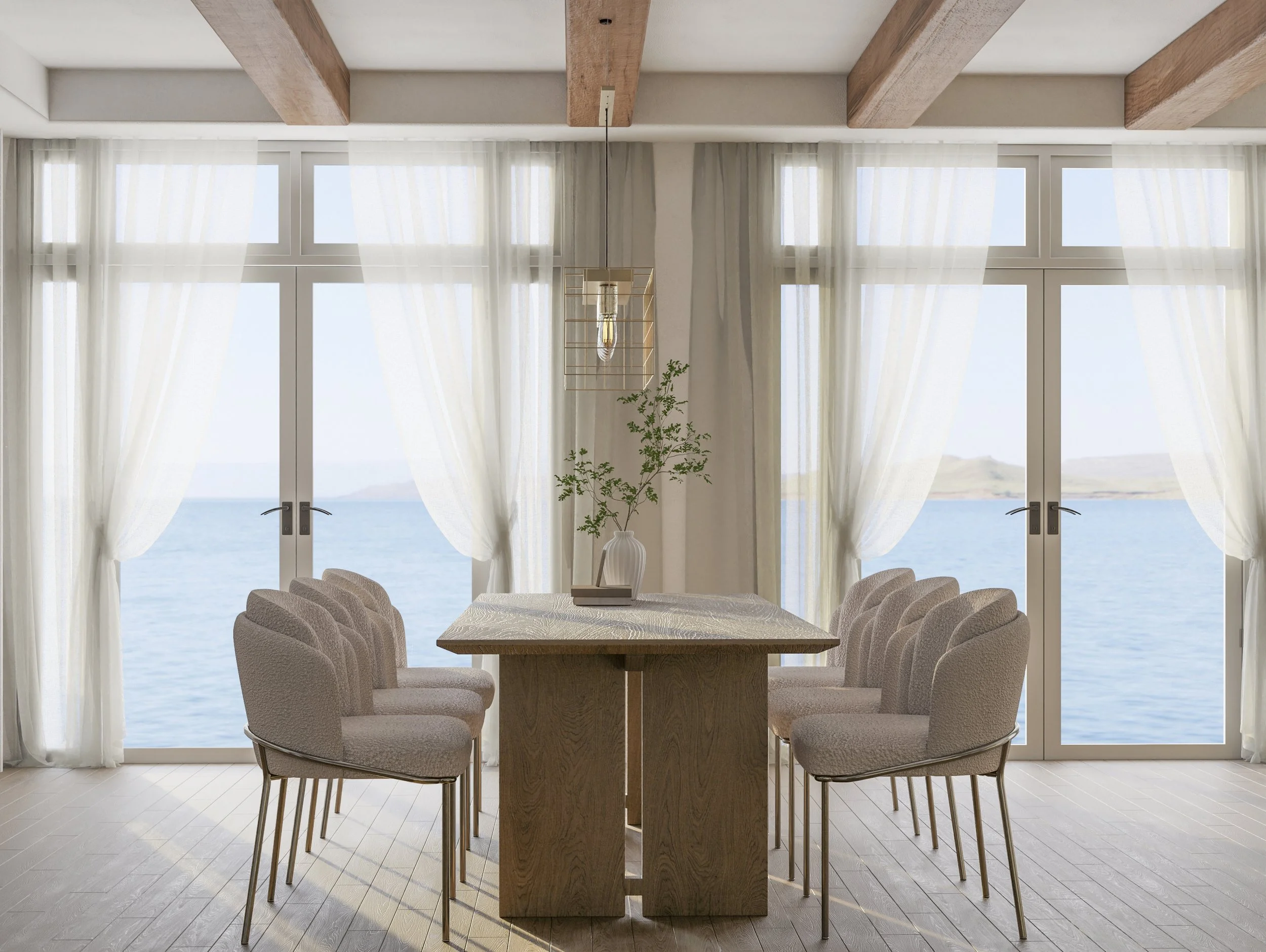A bright, airy dining room with a large wooden table surrounded by twelve beige upholstered chairs. The room has floor-to-ceiling windows showing an ocean view with hills in the distance, and sheer white curtains.