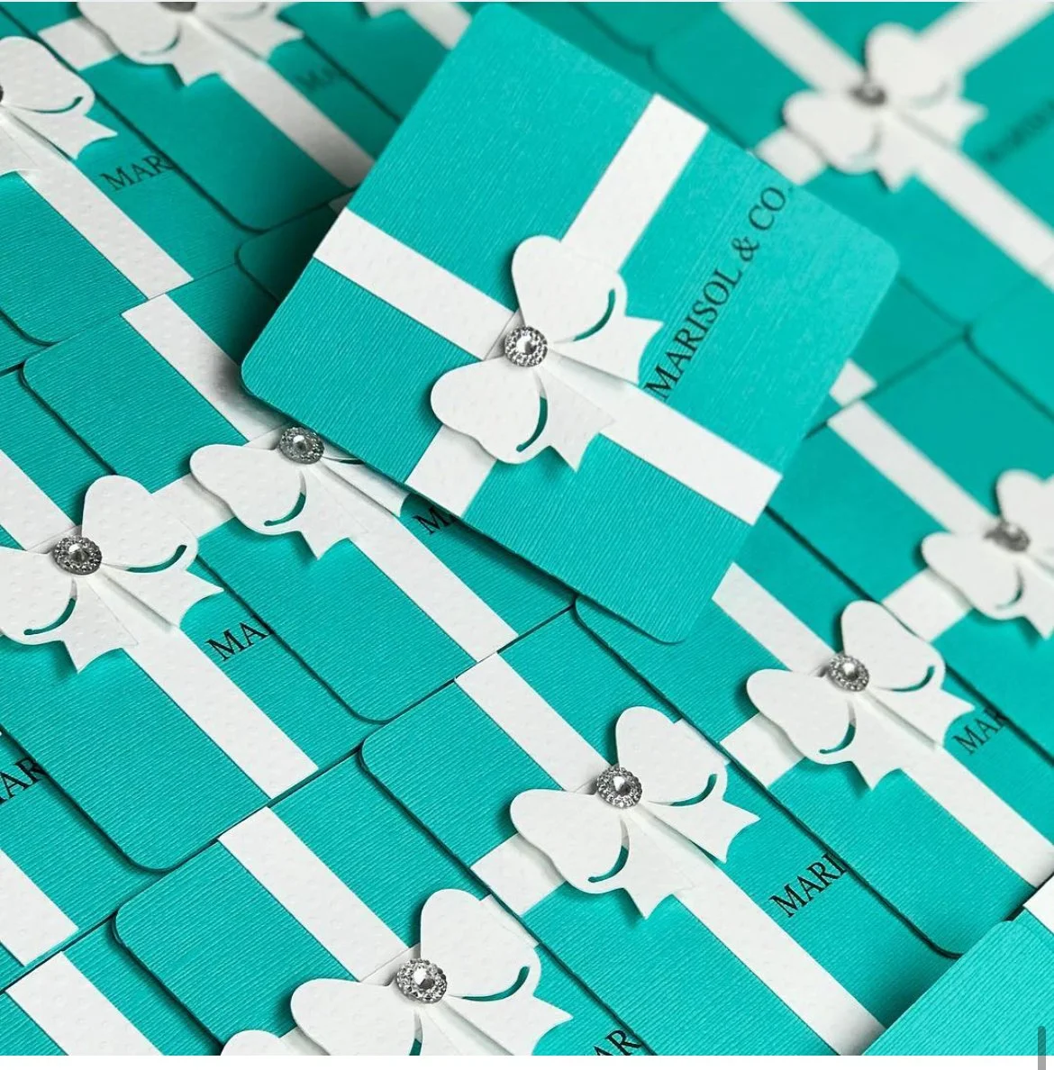 Multiple blue gift boxes with white bows and rhinestone embellishments, labeled 'Marisol & Co.'.