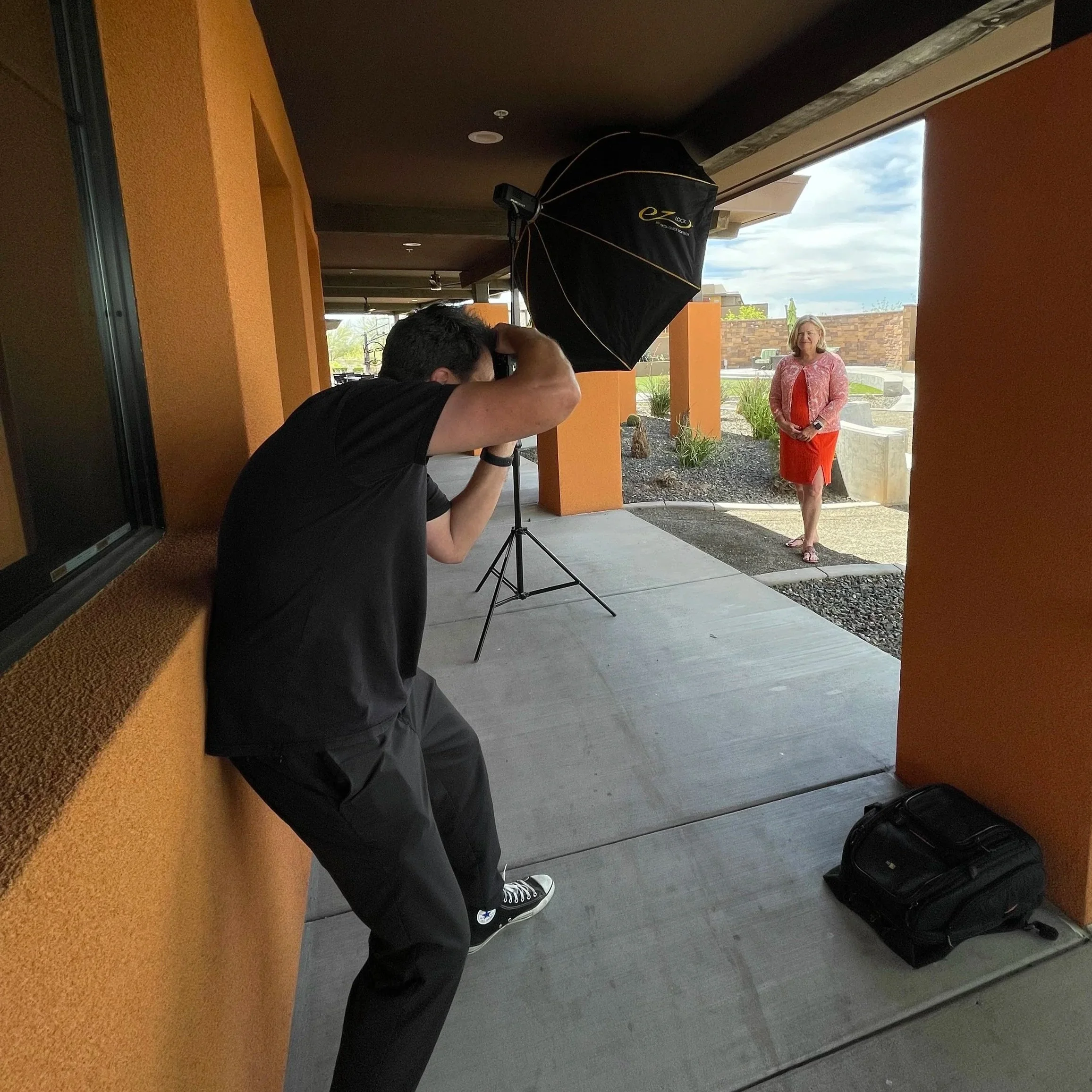 Photographer taking a portrait of a woman standing outside on a patio under a covered walkway.