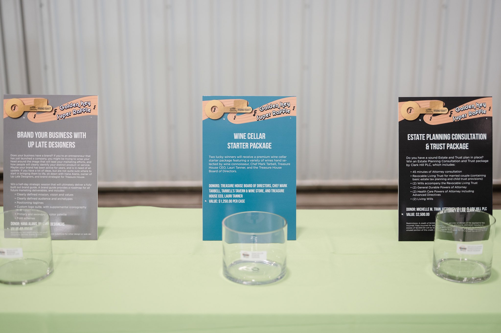 Three informational cards on a light green table, each displayed behind a clear glass, with a metal wall in the background.
