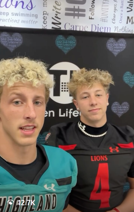 Two young men with blond curly hair are taking a selfie at a Teen Lifetime event. One is wearing a teal sports jersey with 'HIGLAND' on it, and the other is in a black football jersey with the number 4 and 'LIONS' printed on it. They are standing in front of a black background with Teen Lifetime and call-to-action words and blue heart shapes.