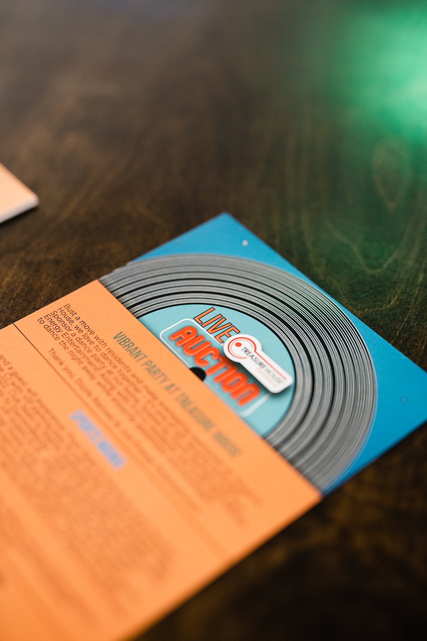 Close-up of a blue and orange flyer or advertisement featuring a vinyl record, with the title "LIVE AUCTION" and text about a vibrant party and dance event.