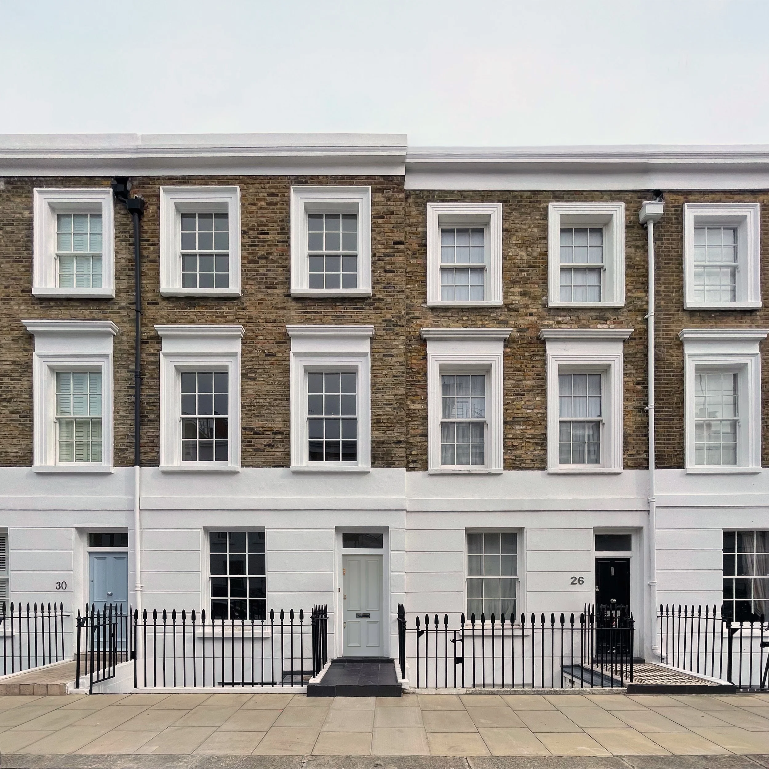 Three-story townhouses with white and brick facades, black fences, and front doors, located on a paved sidewalk.