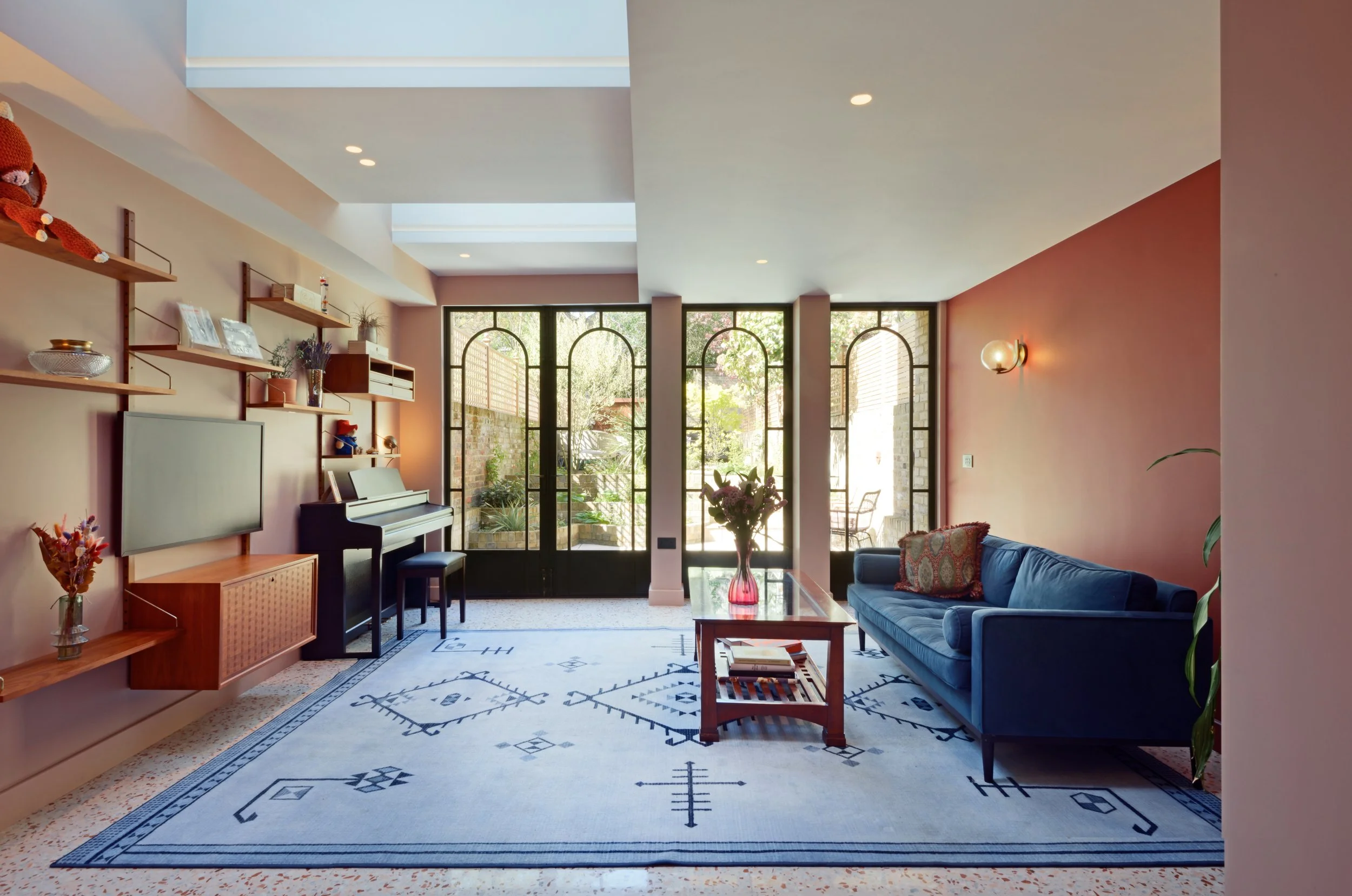 Living room with blue sofa, wooden coffee table with books, patterned rug, and large glass doors opening to an outdoor patio.