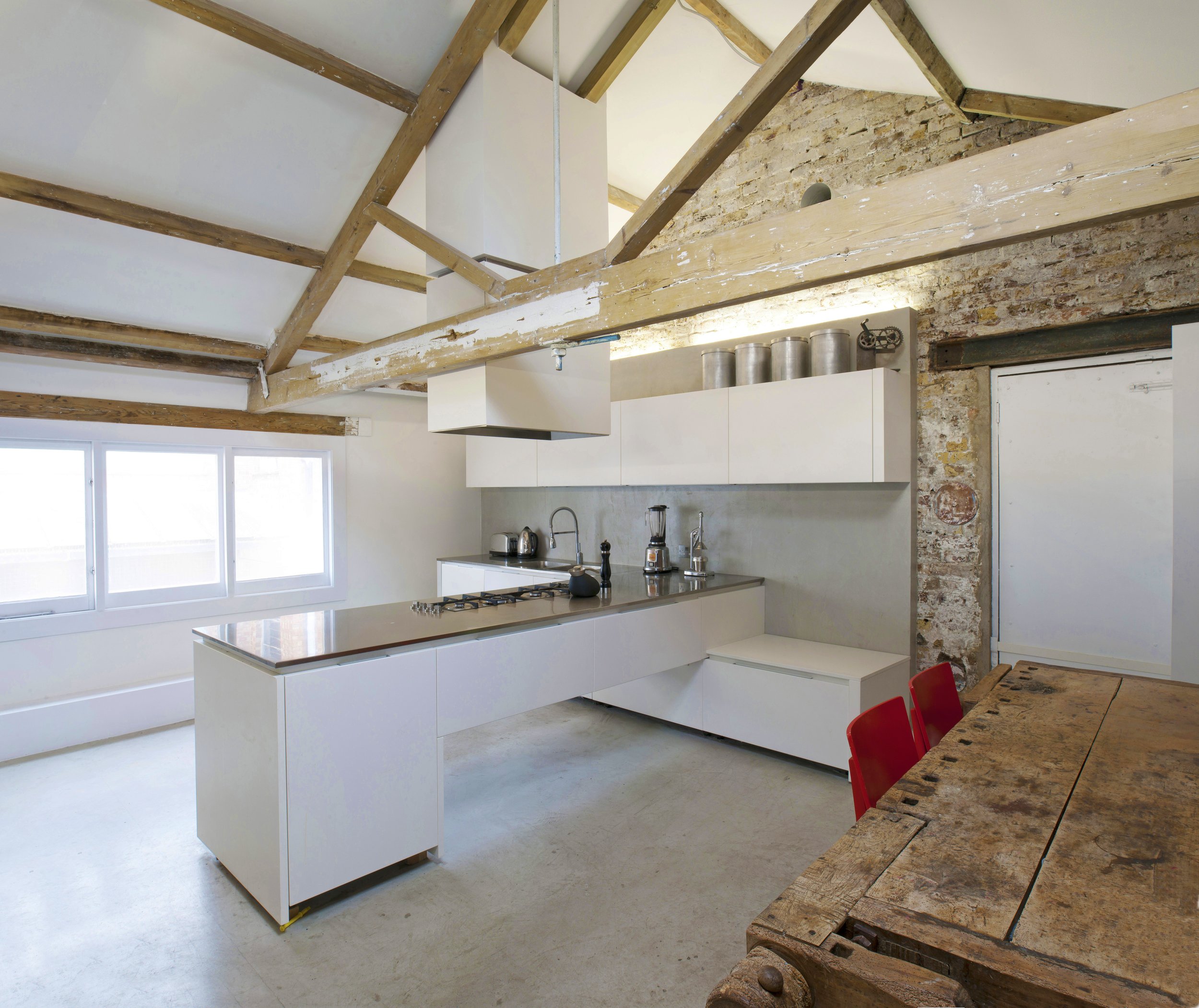 Modern kitchen with white cabinets, stainless steel appliances, and exposed wooden beams in a minimalist-style space with natural light.