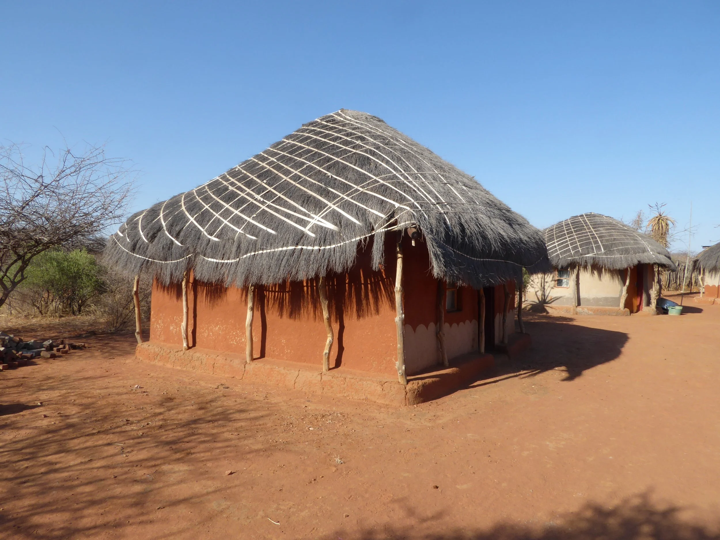 Traditional mud house with thatched roof in a dry, rural landscape.