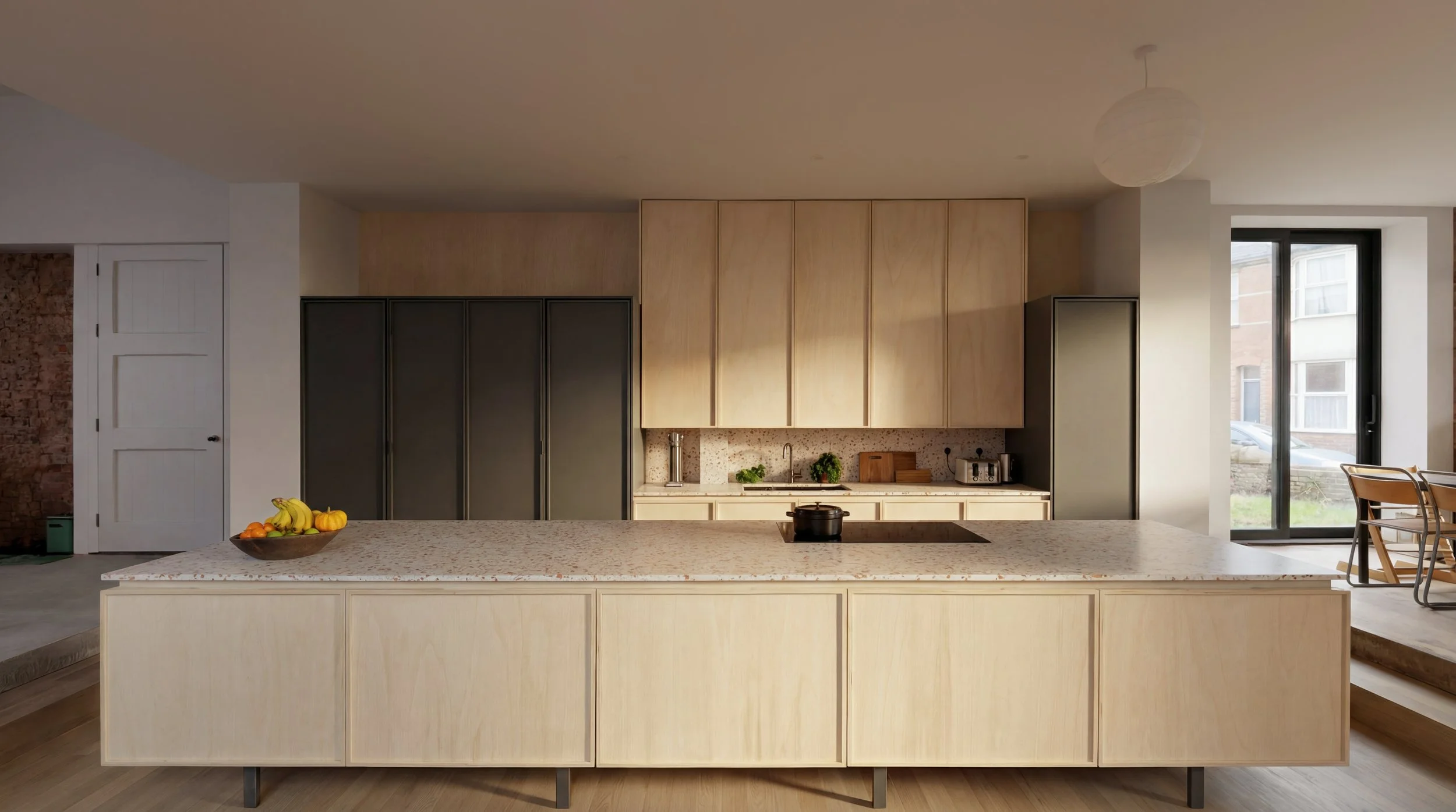 Modern kitchen with a large island counter, fruit bowl, beige cabinets, and a window showing a car outside.