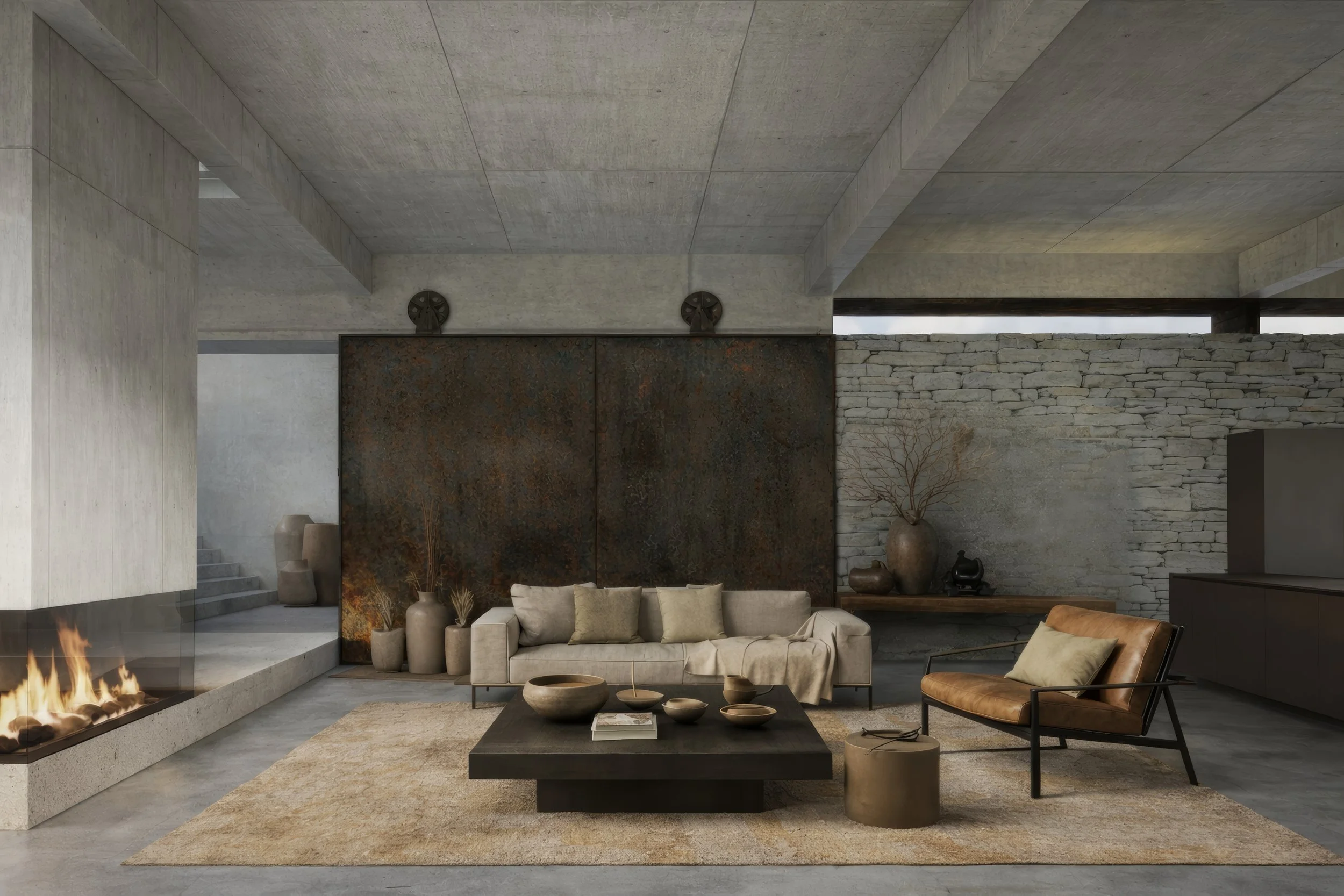 Modern living room with concrete walls and ceiling, a stone fireplace, beige sofa, leather armchair, coffee table with bowls, and decorative vases and branch arrangement.