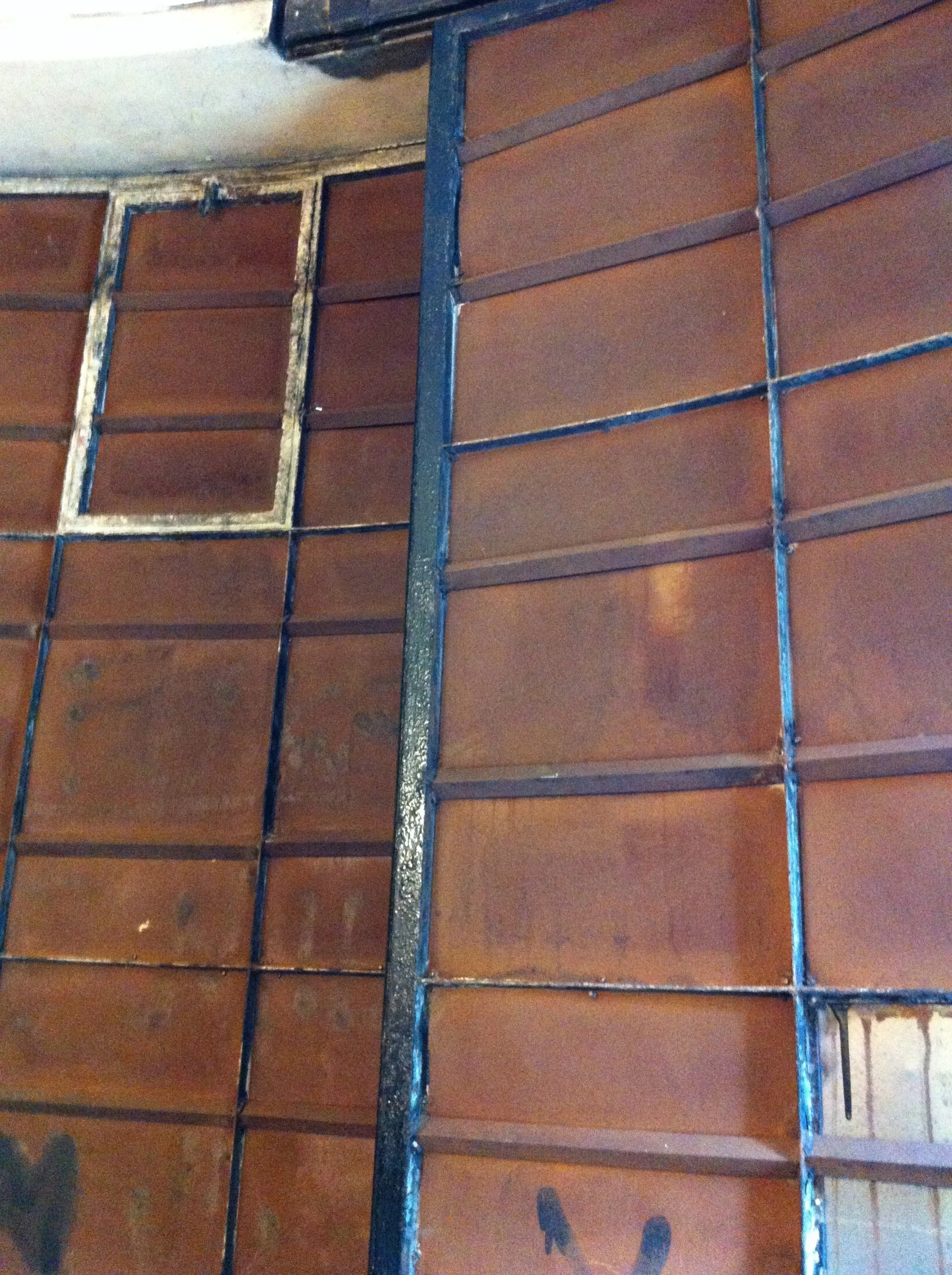 Close-up view of rusty metal rebar grid embedded in concrete wall, with some sections showing oxidation and rust stains.