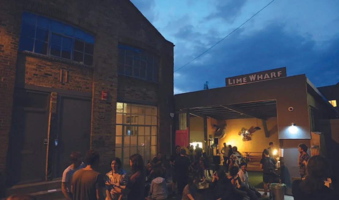 People gather outside a venue called Lime Wharf with an outdoor stage illuminated for a nighttime event.