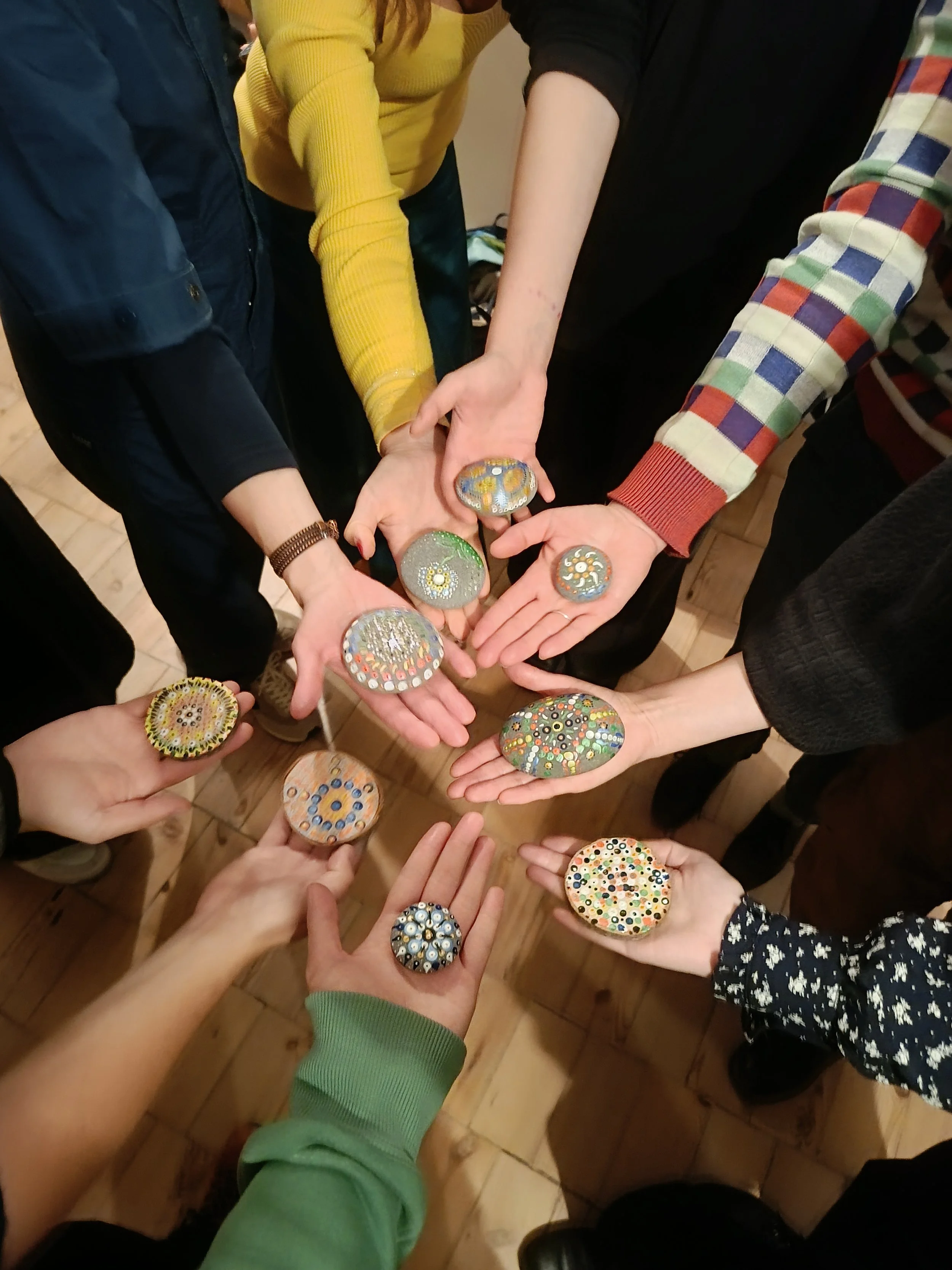 Multiple people holding decorated glass stones with colorful patterns above a wooden floor.