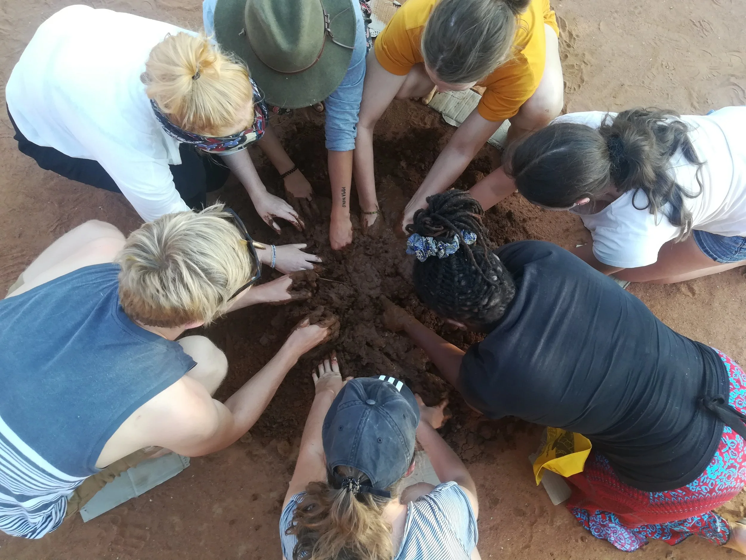 A group of people are gathered in a circle, digging and working together in a hole in the dirt.