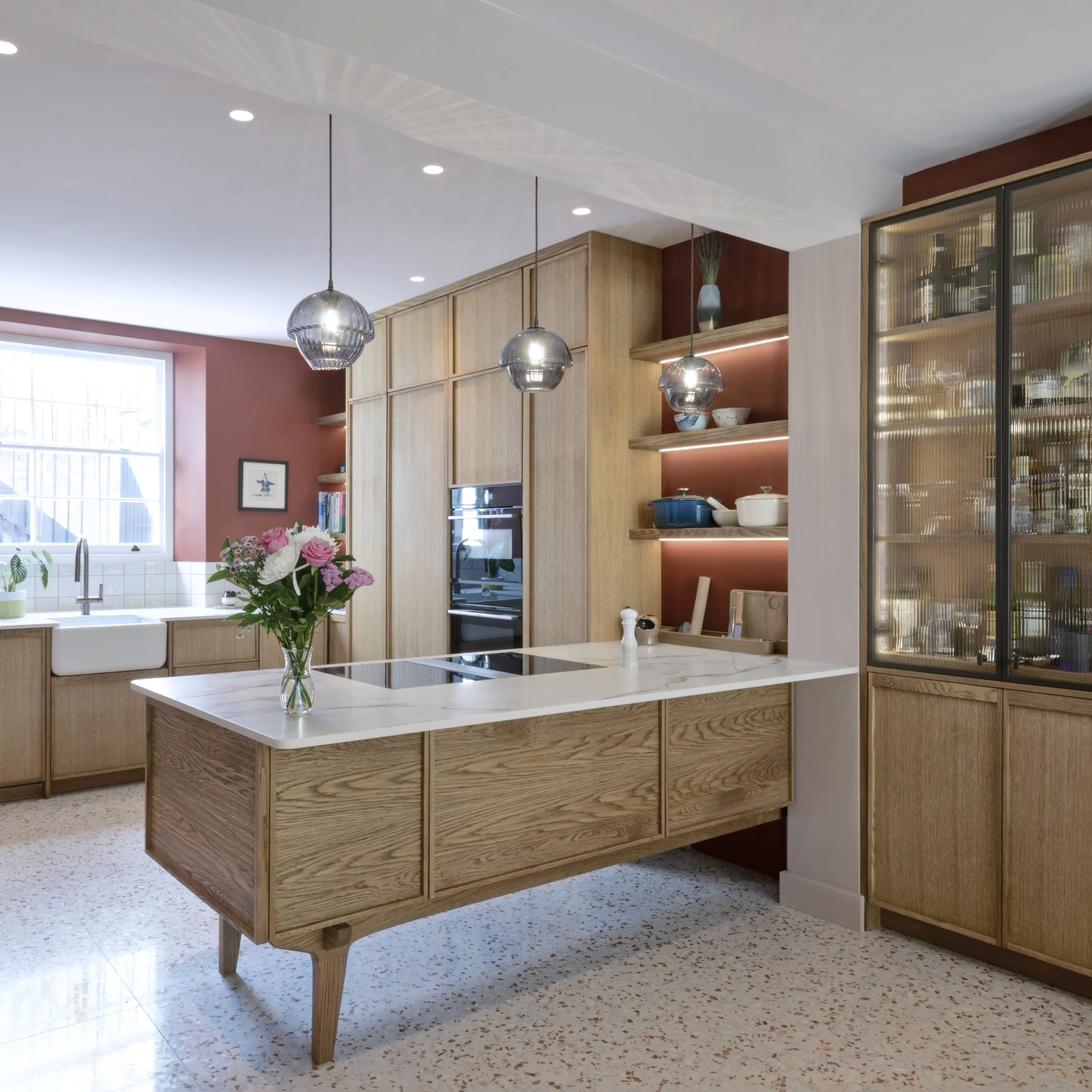 Modern kitchen with wooden cabinetry, marble island, hanging pendant lights, and open shelving displaying dishes and decorative items.