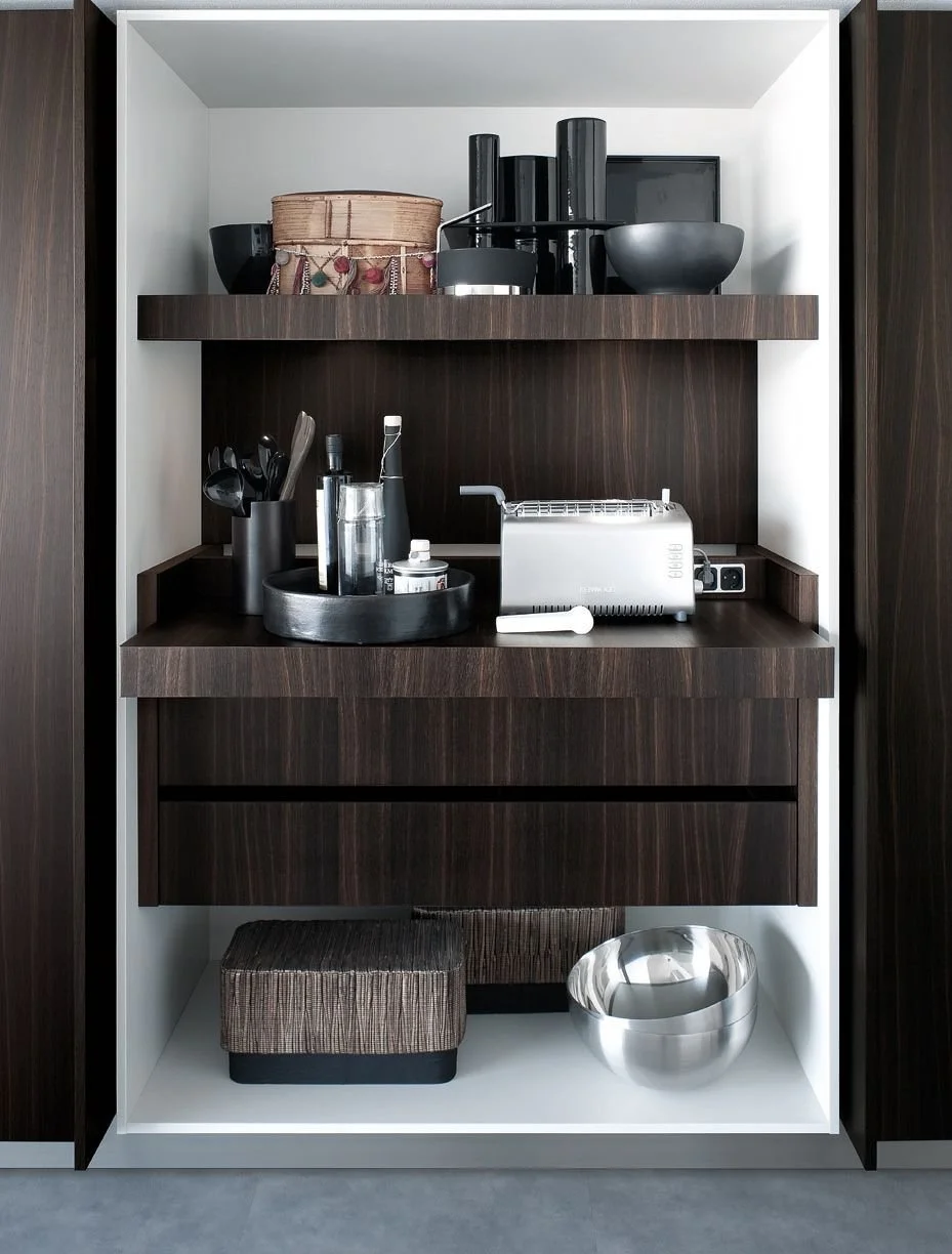 Open cabinet with kitchen items, including black bowls, a woven basket, black bottles, utensils, a toaster, and decorative bowls.